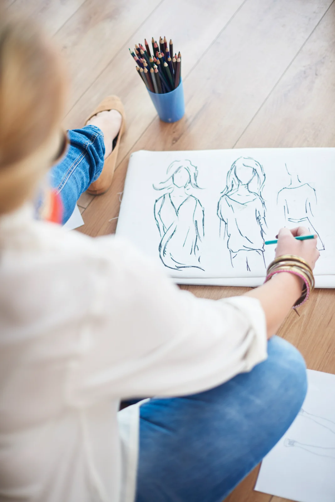 Figure drawing sketches of people on paper beside a cup of pencils