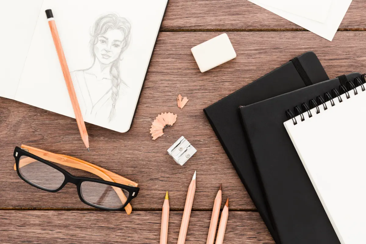 Sketchbook with a pencil portrait, pencils and an eraser on a wooden desk